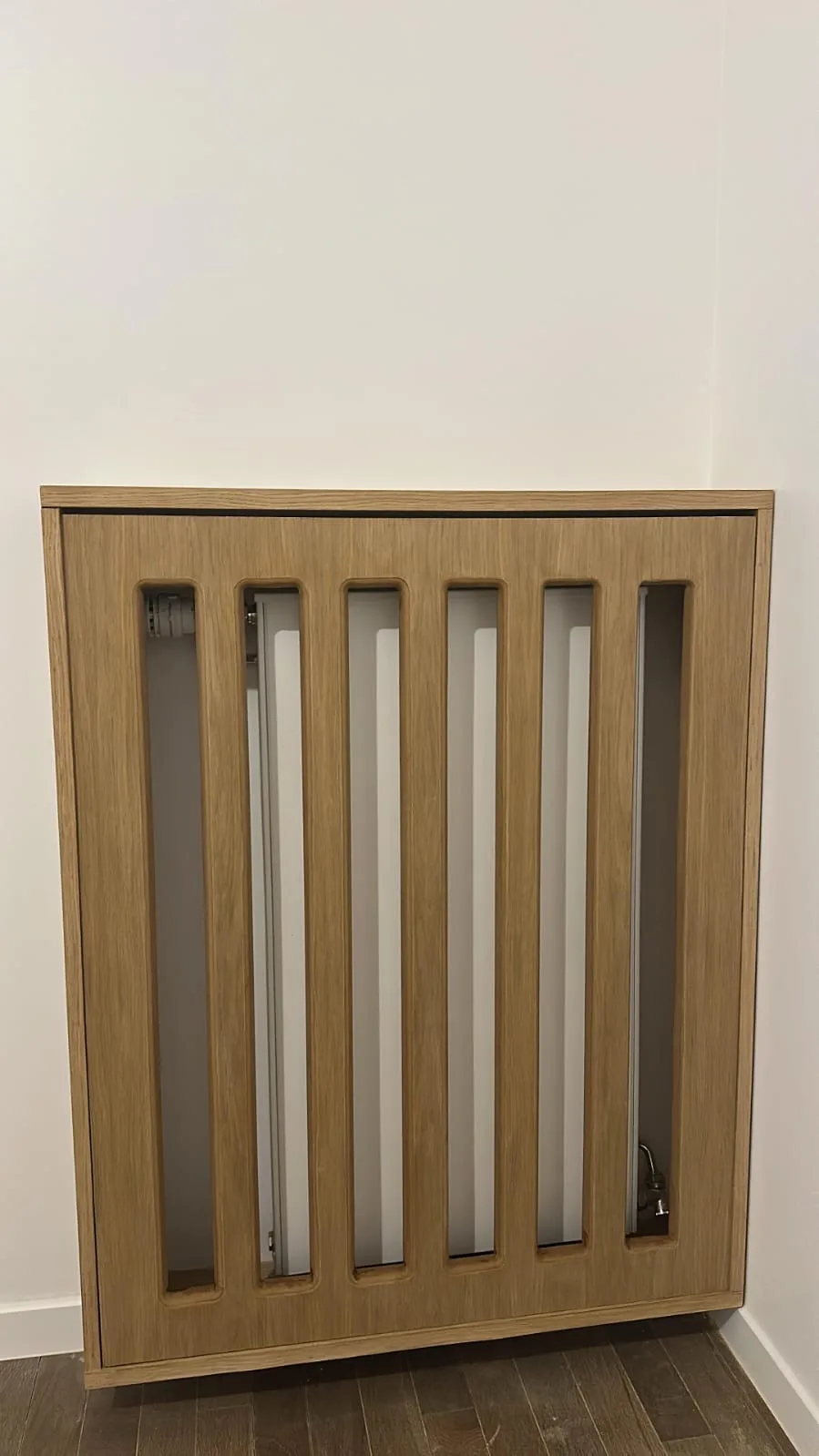 Cache-radiateur sur mesure en chêne à claire-voie, avec fentes verticales à angles arrondis, posé contre un mur blanc