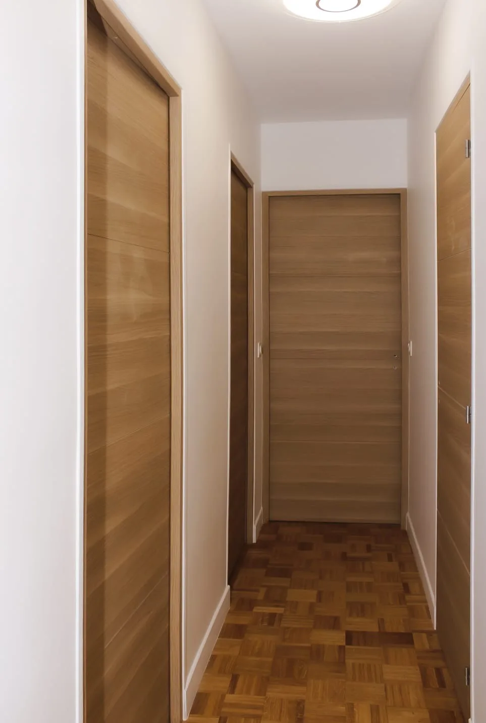 Couloir d'appartement avec portes et huisseries plaquées chêne, parquet mosaïque et murs peints en blanc