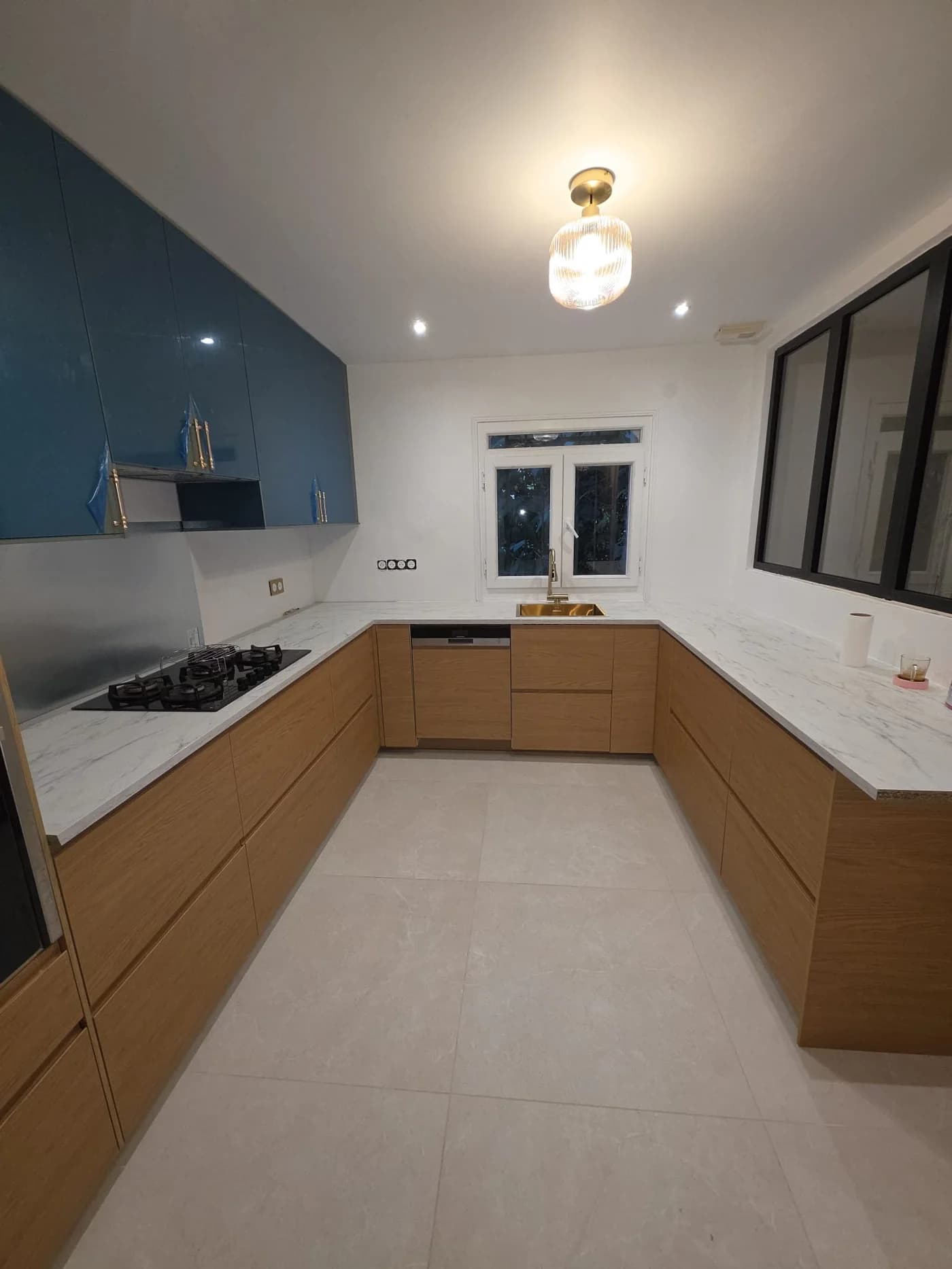 Cuisine en U sur mesure avec façades en chêne, meubles hauts laqués bleu, crédence inox et verrière noire