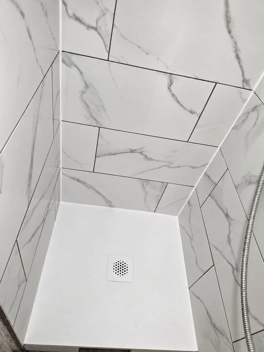 Douche à l'italienne carrelée en faïence effet marbre, avec receveur extra-plat blanc et bonde carrée centrée