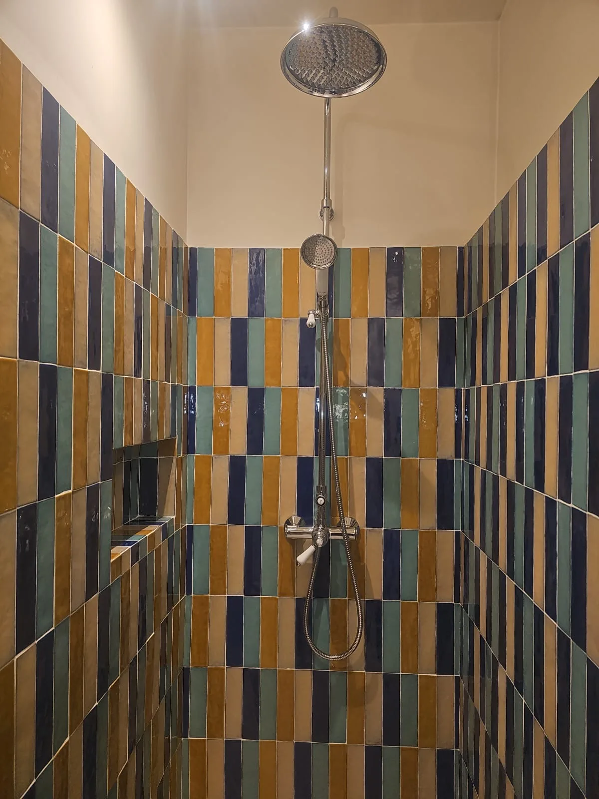 Douche à l'italienne entièrement habillée de zellige bleu, vert et jaune, avec niche intégrée et colonne de douche murale