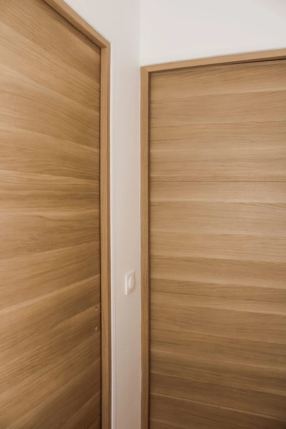 Détail de deux portes plaquées chêne dans un angle, avec huisseries habillées et interrupteur encastré