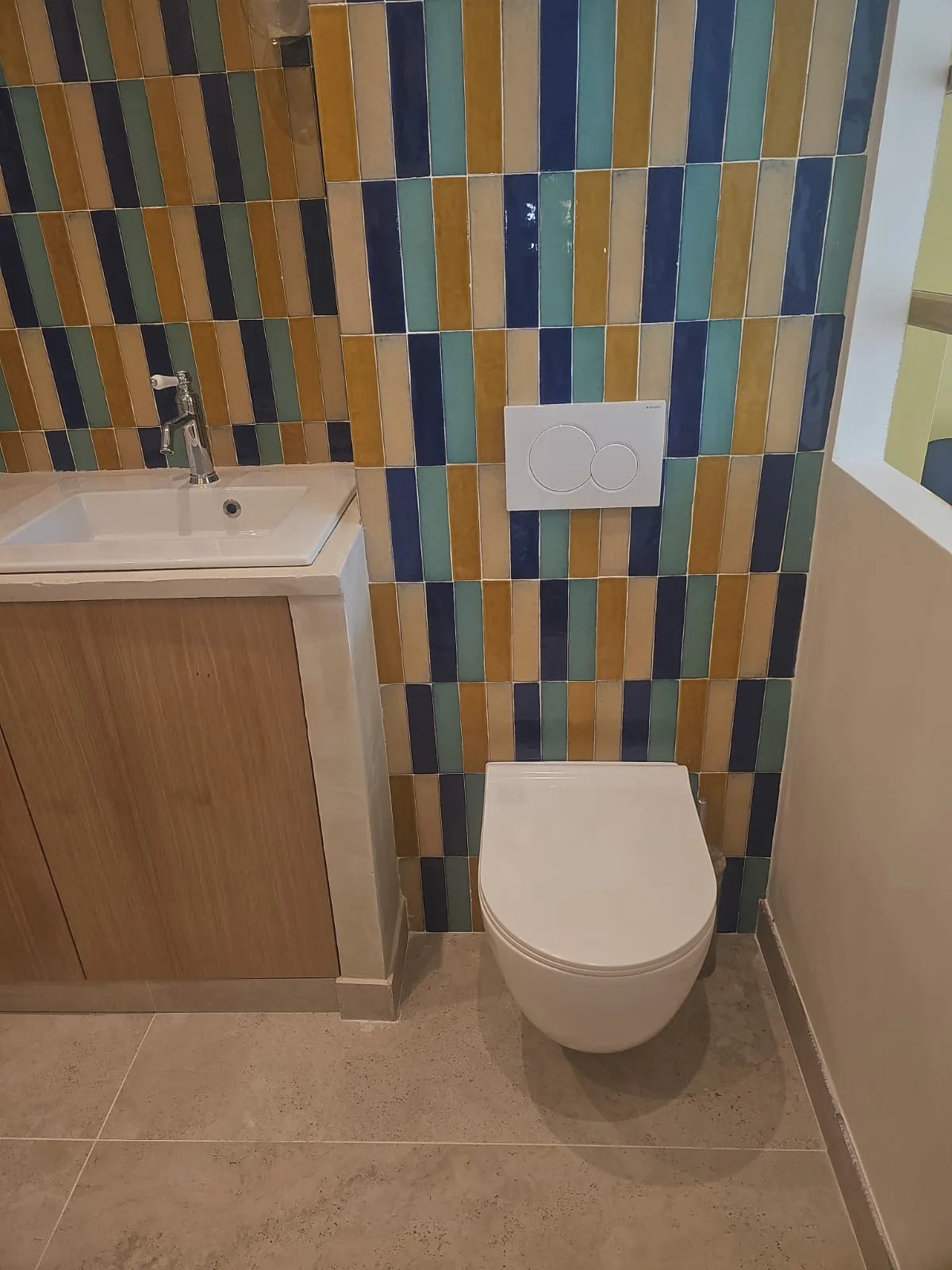 WC suspendu devant un mur en zellige coloré, à côté d'un meuble vasque sur mesure en chêne