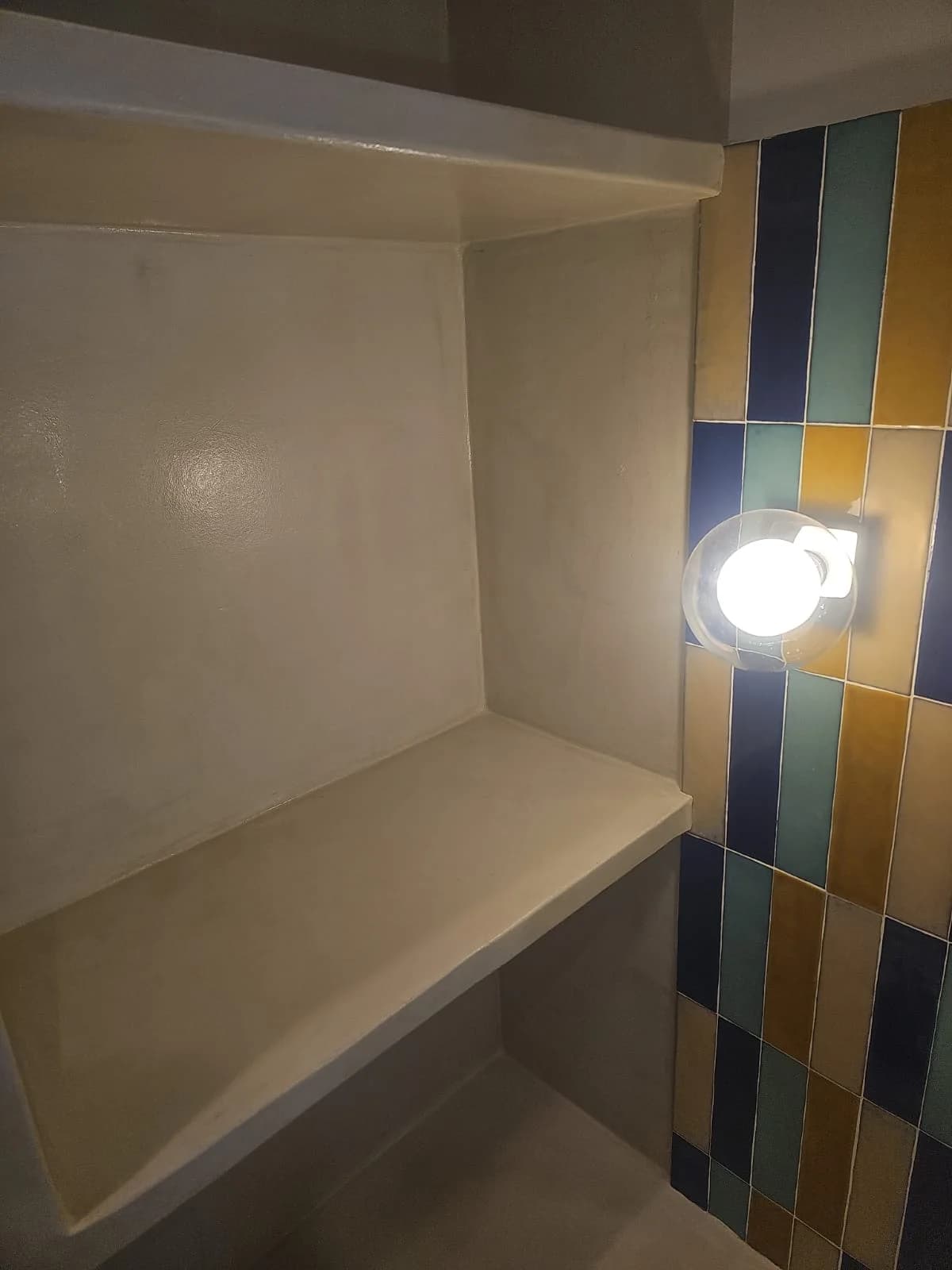 Banc maçonné en béton ciré dans la douche, bordé du même zellige coloré